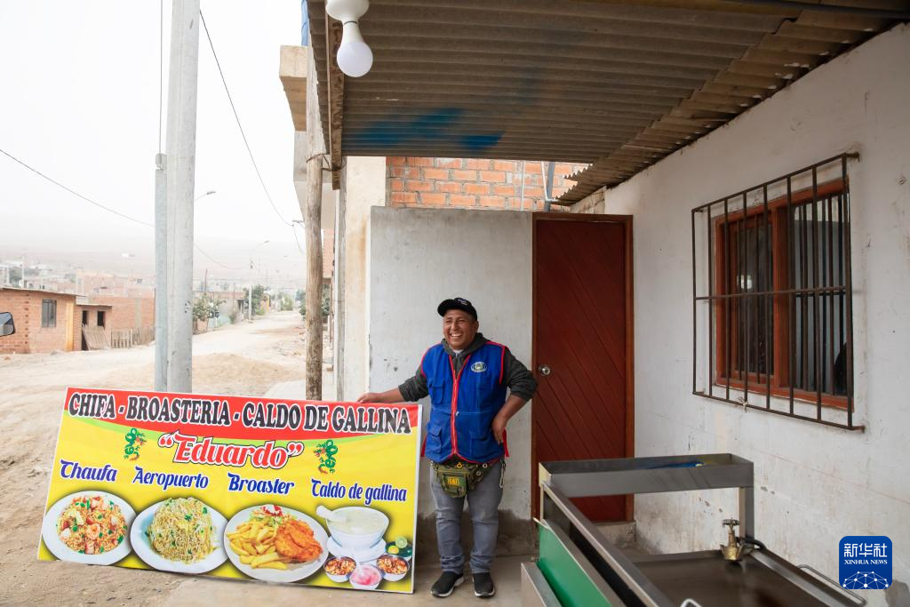   8月14日，在位于秘鲁首都利马城区以北的阿斯普罗丹社区，当地居民爱德华多·坎查诺展示他的美食招牌。新华社发（玛丽安娜·巴索摄）